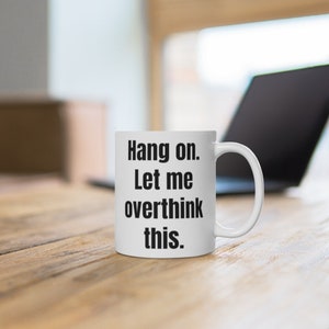K&ouml;nnte beinhalten: Eine wei&szlig;e Keramik-Kaffeetasse mit schwarzem Text, der "Hang on. Let me overthink this." lautet.