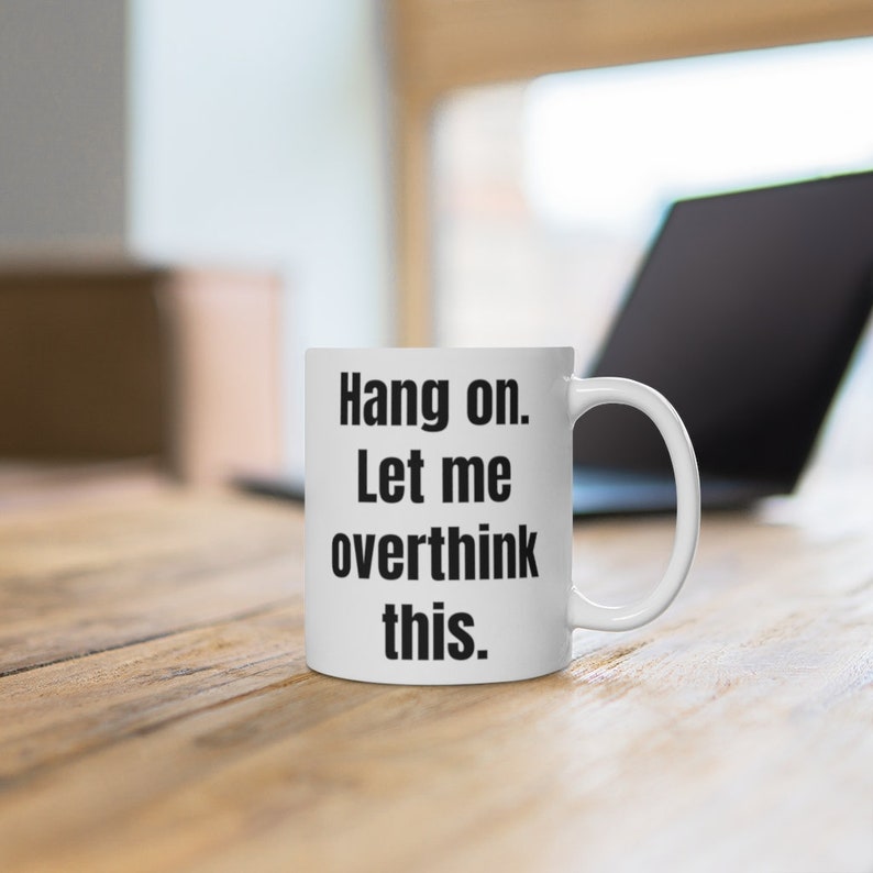 K&ouml;nnte beinhalten: Eine wei&szlig;e Keramik-Kaffeetasse mit schwarzem Text, der "Hang on. Let me overthink this." lautet.