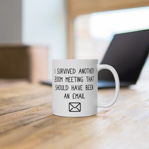 May include: White ceramic coffee mug with black text that reads "I survived another zoom meeting that should have been an email" and a black envelope icon.