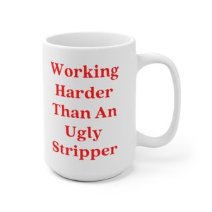 May include: White ceramic coffee mug with a red inscription that reads "Working Harder Than An Ugly Stripper".