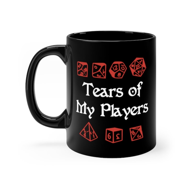 以下が含まれることがあります： 白い文字で「Tears of My Players」と赤いサイコロのグラフィックが描かれた黒いセラミック製のコーヒーカップです。