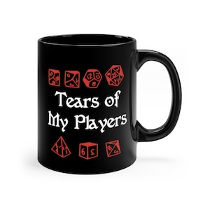 以下が含まれることがあります： 黒いセラミック製のコーヒーカップ。白い文字で「Tears of My Players」と書いてあり、その周りに赤いサイコロのアイコンが並んでいます。