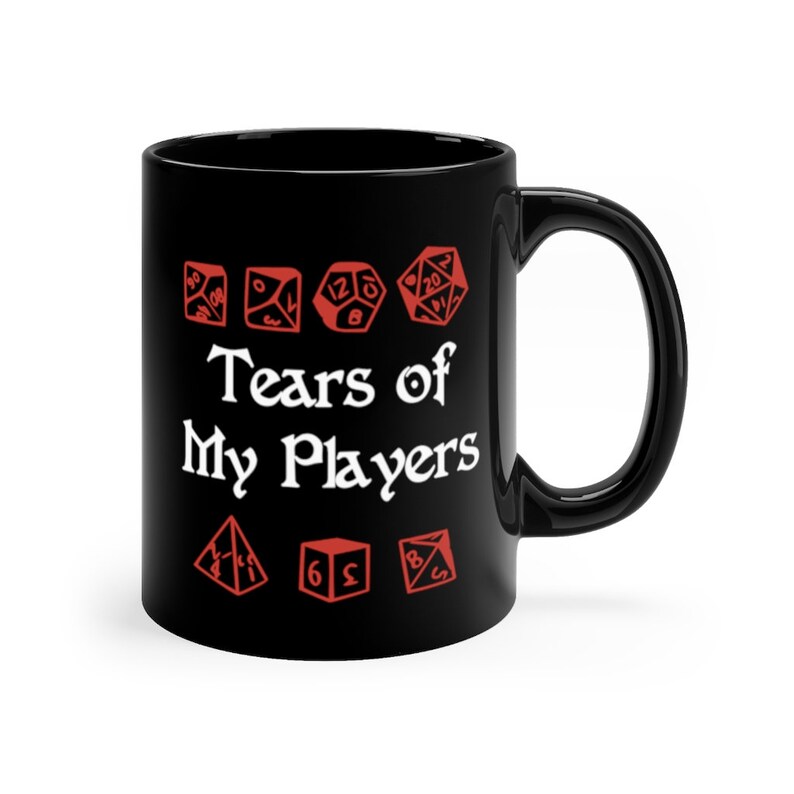 以下が含まれることがあります： 黒いセラミック製のコーヒーカップ。白い文字で「Tears of My Players」と書いてあり、その周りに赤いサイコロのアイコンが並んでいます。