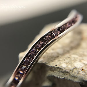 May include: A silver band with a row of small, light purple gemstones set in a curved design.