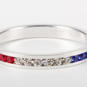 May include: A silver band ring with a row of red, clear, and blue crystals.