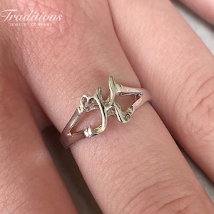 Puede incluir: Un anillo de plata con un diseño de letra cursiva 'J'. El anillo está en un dedo.