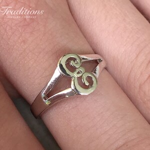 May include: A silver ring with a stylized double-loop design. The ring is worn on a finger.