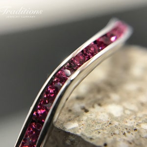 Könnte beinhalten: Nahaufnahme einer silbernen Band mit einer Reihe von rosafarbenen Edelsteinen. Die Band ist gebogen und die Edelsteine sind in einer Kanalfassung gefasst.