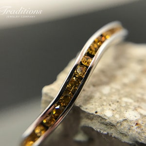 May include: A thin silver band with a row of small, golden gemstones set in a curved pattern.
