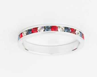 May include: A silver ring with a band of alternating red, white, and blue gemstones. The ring is set against a white background, highlighting the colors of the gemstones. The ring is a piece of jewelry.