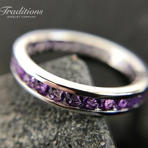 Puede incluir: Un anillo de banda de plata con una fila de piedras preciosas de amatista púrpura engastadas en un engaste de canal.