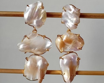 May include: A pair of gold-tone earrings with three white and cream baroque pearls on each earring. The pearls are wired together and have an irregular shape.