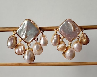 May include: A pair of gold earrings with a large, white, iridescent, pearlescent, square-shaped stone in the center. The earrings have five smaller, white, pearlescent stones hanging from the bottom of the larger stone.