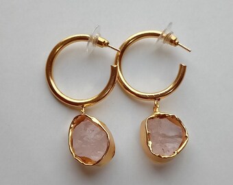 May include: A pair of gold hoop earrings with a pink crystal charm hanging from each hoop.