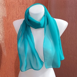 Può includere: Una sciarpa di chiffon blu turchese drappeggiata su un manichino bianco.