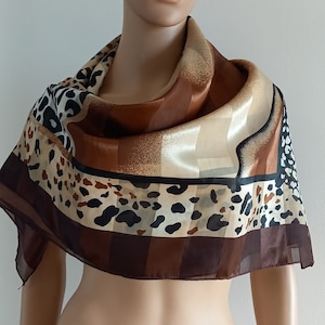 Könnte beinhalten: Ein brauner, beiger und schwarzer gemusterter Seidenschal mit Leopardenmuster. Der Schal ist gefaltet und um den Hals einer Person gelegt.