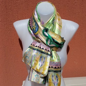 May include: A colourful silk scarf with a paisley pattern in shades of green, gold, purple, and black. The scarf is draped around a white mannequin.