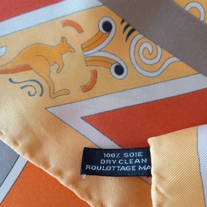 May include: A yellow silk scarf with a geometric pattern featuring a kangaroo, a brown and white label with the text "100% SOIE DRY CLEAN ROULOTTAGE MA"