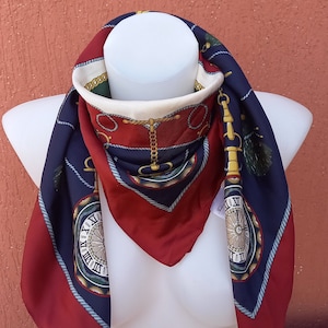 May include: A square silk scarf in navy blue, burgundy, and cream. It features a clock face design, gold chains, and rope detailing. The scarf is displayed on a white mannequin. The scarf measures approximately 90cm x 90cm.