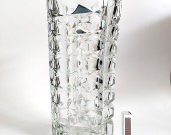 May include: A clear, faceted glass vase with a rectangular shape and a textured surface. The vase is approximately 10 inches tall. A matchbox is next to the vase for scale.