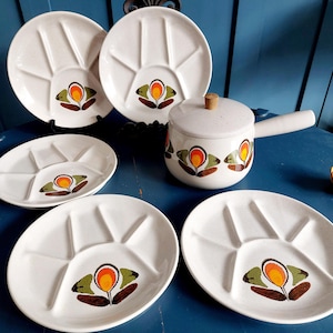 May include: A vintage white ceramic serving set with a floral design. The set includes plates with divided sections and a small pot with a handle and lid. The floral design features orange, yellow, and brown colors.