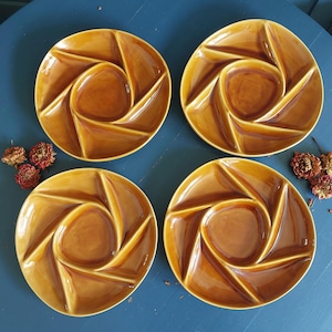 Può includere: Quattro piatti da portata vintage in ceramica marrone. Ogni piatto ha un pozzetto centrale circolare circondato da sei scomparti triangolari, creando un motivo a spirale. I piatti sono disposti su una superficie blu, con fiori secchi.