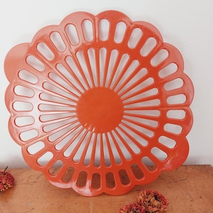 Könnte beinhalten: Orangefarbener Serviertablett aus Kunststoff mit einem gewellten Rand und einem Sonnenstrahl-Design. Das Tablett hat ein dekoratives durchbrochenes Muster.