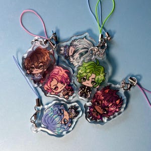 May include: Six colorful anime character charms with clear plastic backgrounds and attached strings. The charms feature different characters with various hair colors and styles, including green, blue, pink, brown, and white.