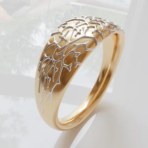 Könnte beinhalten: Ein goldener Ring mit einem filigranen, kunstvollen Design eines Baumzweigs in Silber. Der Ring ist poliert und hat eine glatte Oberfläche.