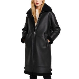 Könnte beinhalten: Langer schwarzer Kunstleder-Mantel mit schwarzem Shearling-Kragen und -Besatz. Der Mantel hat einen Reißverschluss, Taschen und ein klassisches Design. Der Mantel ist knielang und wirkt warm und stilvoll.