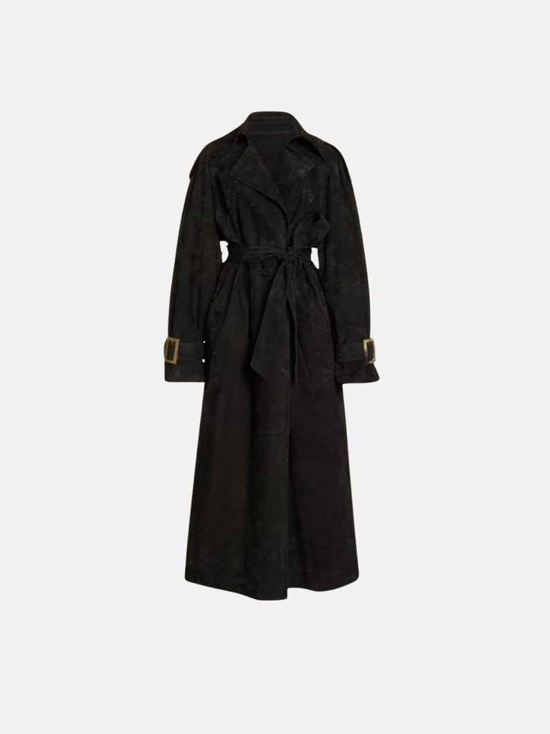 May include: A long black trench coat featuring a wide notched collar, long sleeves with buckled cuffs, and a matching tie belt at the waist. The coat has a textured finish and falls to a midi length, providing a structured and classic silhouette.