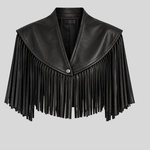 Puede incluir: Una chaqueta negra corta con cuello ancho y largos flecos a lo largo del dobladillo y las mangas. La prenda cuenta con un cierre de bot&oacute;n a presi&oacute;n plateado en el centro delantero y un acabado liso y estructurado en toda la pieza.