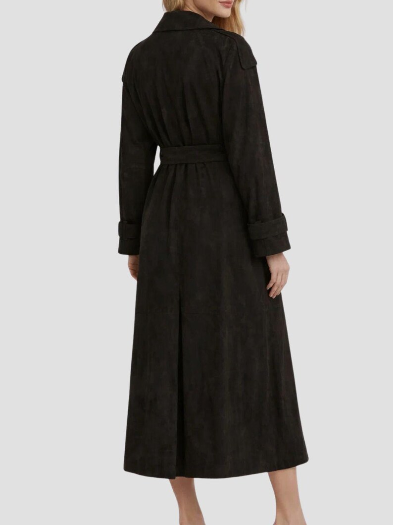 May include: A long, dark brown trench coat featuring a collared neckline, long sleeves with cuff straps, and a matching tie belt at the waist. The coat has a structured shoulder design and a single back vent, extending down to the lower calf area.