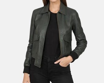 May include: A dark forest green leather jacket featuring a classic collar, a central front zipper, and two large flap pockets on the chest. The jacket has long sleeves with black ribbed cuffs and a matching black ribbed hem at the waistline.