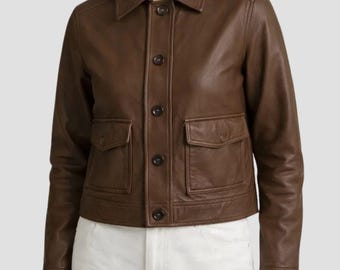 May include: A brown leather jacket featuring a classic collar, a front button-down closure with dark buttons, and two square chest pockets with buttoned flaps. The jacket has long sleeves with buttoned cuffs and a straight hemline.