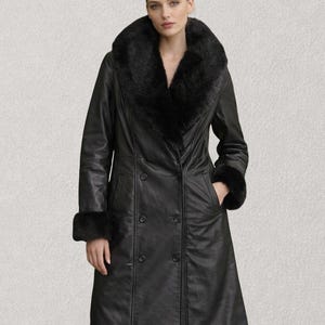 K&ouml;nnte beinhalten: Ein schwarzer Ledermantel mit einem Kunstfellkragen und Manschetten. Der doppelreihige Mantel hat eine lange L&auml;nge und ein klassisches Design. Der Mantel hat zwei Taschen und eine taillierte Passform, geeignet f&uuml;r kaltes Wetter.