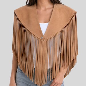 Puede incluir: Un poncho de ante color tostado con un escote en V profundo y un cierre de botón a presión plateado. La prenda está adornada con largos flecos verticales que se extienden desde los hombros hasta el dobladillo, creando un efecto de capas.