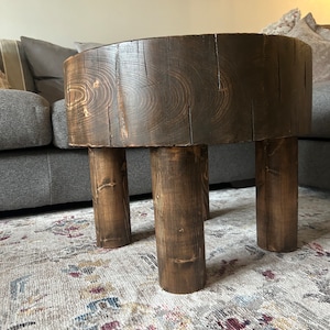 May include: A dark brown wooden coffee table with a round top and four legs. The table is made from a single piece of wood and has a rustic, natural look.