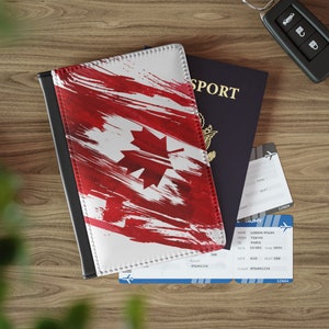 May include: A passport holder with a red and white Canadian flag design. The holder is made of leather and has a black border. The holder is lying on a wooden table next to a passport and two airline boarding passes.