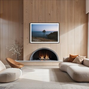 May include: A modern living room with a fireplace, a large framed landscape art piece, and a curved sofa. The room features light-colored walls, a neutral rug, and large windows with sheer curtains. Two chairs are in the foreground.