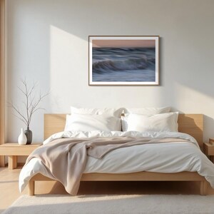 May include: A bedroom with a large window, a bed with white linens and a brown throw blanket, and a framed photograph of ocean waves on the wall.