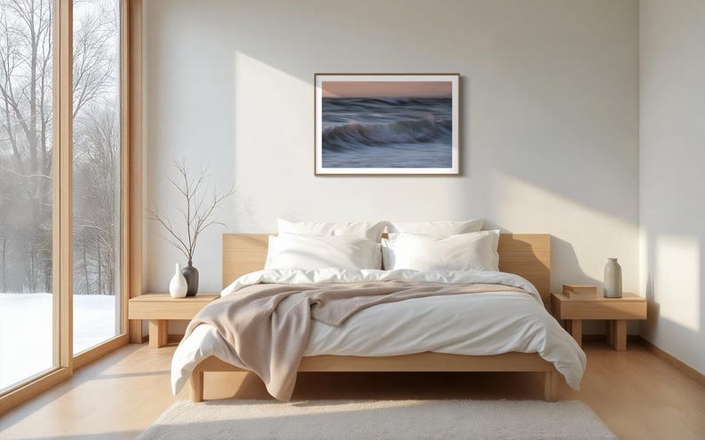 May include: A bedroom with a large window, a bed with white linens and a brown throw blanket, and a framed photograph of ocean waves on the wall.