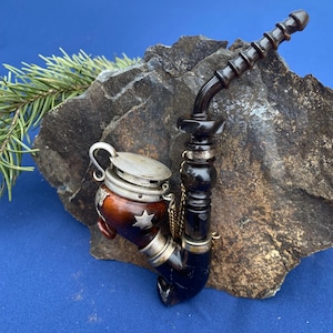May include: An antique tobacco pipe with a dark wooden stem and bowl. The bowl is a combination of brown and blue with a silver lid and star design. A silver chain connects the lid to the pipe.