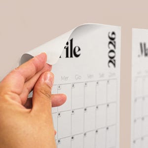 Könnte beinhalten: Ein weißer Kalender mit schwarzem Text, der das Jahr 2026 zeigt. Die Ecke des Kalenders wird abgezogen und zeigt den Monat "ile". Der Kalender hat ein Raster aus Quadraten für jeden Tag.