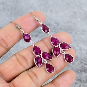May include: A pair of dangle earrings with multiple ruby-colored gemstones. The earrings are made of sterling silver and have a teardrop shape.