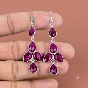 Puede incluir: Un par de pendientes colgantes de plata con piedras preciosas de color rosa intenso facetadas en forma de lágrima. Cada pendiente consta de una piedra superior conectada a un grupo de tres piedras en la base, suspendidas de un gancho de plata.