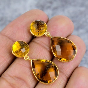 May include: A pair of gold tone earrings with teardrop shaped topaz gemstones. The earrings have a smaller round topaz gemstone at the top of the teardrop.