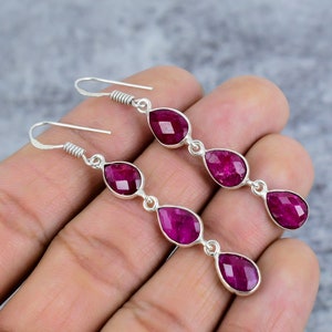 Könnte beinhalten: Ein Paar silberne Ohrhänger mit drei tropfenförmigen Rubinen. Die Ohrringe haben ein schlichtes Design und sind perfekt für den Alltag.