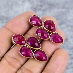 May include: A pair of earrings with five ruby-colored stones set in gold. The stones are faceted and have a teardrop shape. The earrings are a cluster of stones.
