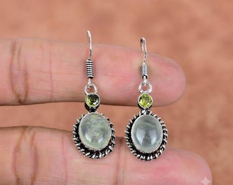 May include: A pair of silver dangle earrings featuring oval-shaped, translucent light green cabochon stones set in twisted metal frames, topped with small, round, faceted lime green stones and silver hook-style ear wires for attachment.